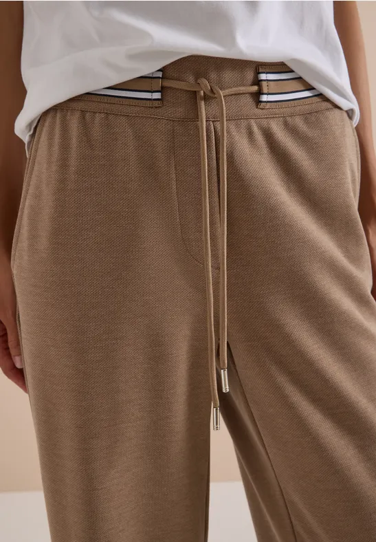 Person trägt beige Jogginghose mit Tunnelzug und Streifen an der Taille.