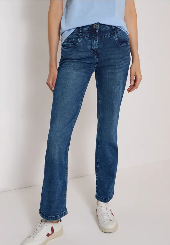 Person trägt gerade geschnittene blaue Jeans und weiße Sneaker, Hintergrund hell.