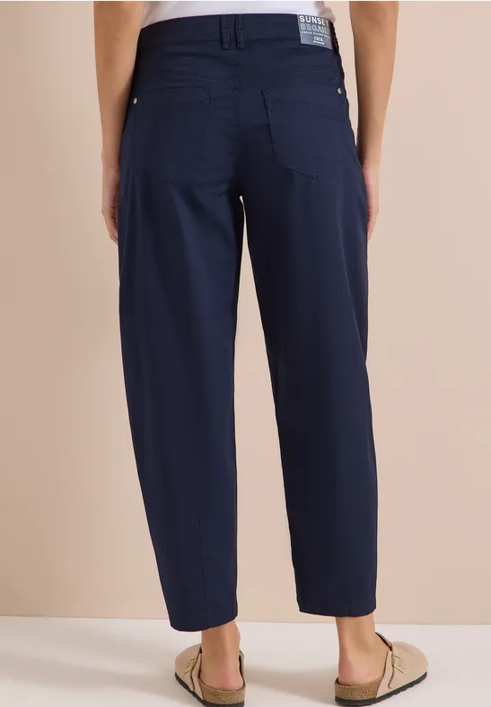 Personne de dos portant un pantalon bleu marine décontracté arrivant aux chevilles et des sandales.