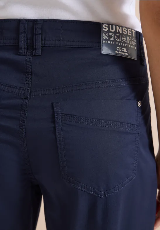 Vue arrière d'une personne portant un pantalon bleu marine avec poches et un haut blanc.