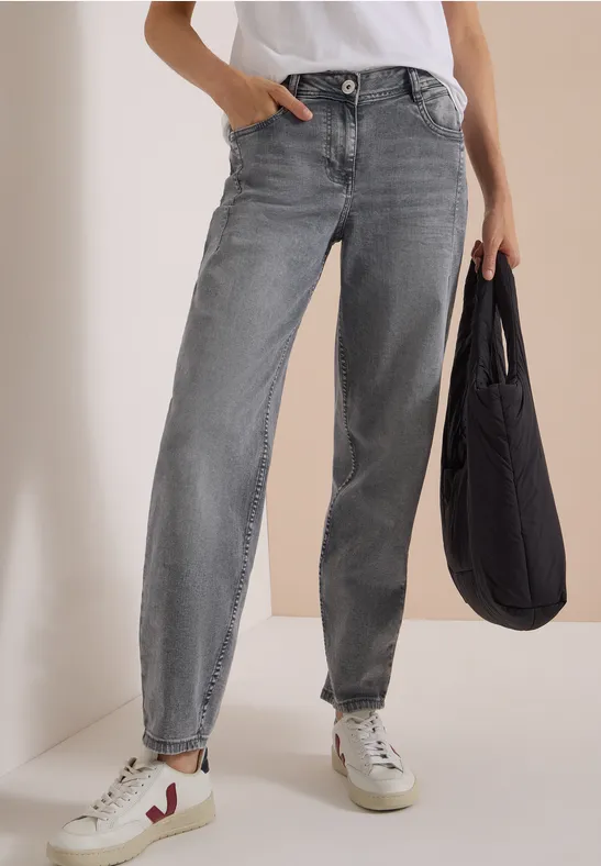 Frau trägt graue Jeanshose, weiße Sneaker und hält eine schwarze Tasche.