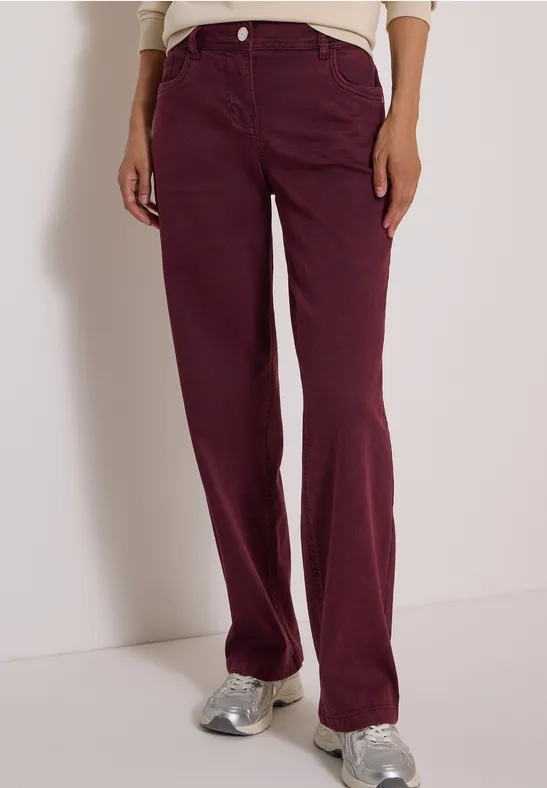 Une personne porte un jean bordeaux taille haute, coupe droite, et des baskets argentées.