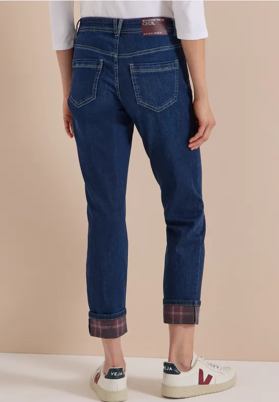 Vue arrière d'une personne portant un jean bleu foncé à revers à carreaux et des baskets blanches.