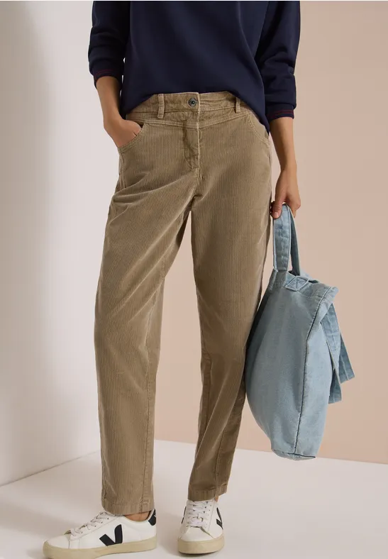 Person trägt hellbraune Cordhose und weiße Sneaker, hält eine blaue Jeansjacke.