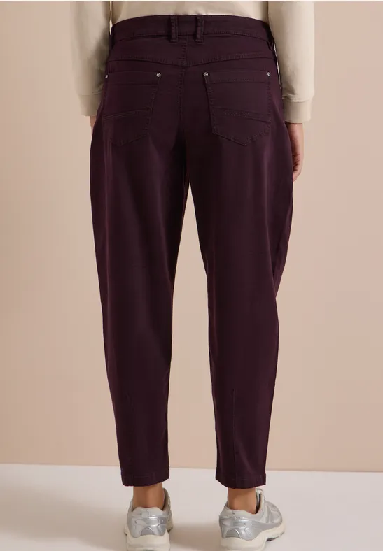 Rückansicht einer Person in lässigen, dunkelvioletten High-Waist-Hosen und weißen Sneakern.