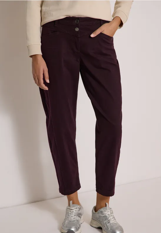 Damenhose in dunklem Aubergine mit umgeschlagenen Säumen, kombiniert mit Sneakern und hellem Pullover.