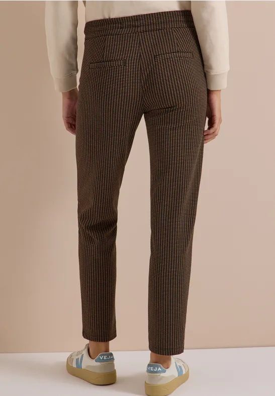 Vue de dos d’une personne portant un pantalon marron à carreaux et des baskets pastel.