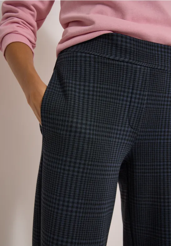 Nahaufnahme einer Person in karierter Hose und rosa Pullover, Hand in Tasche