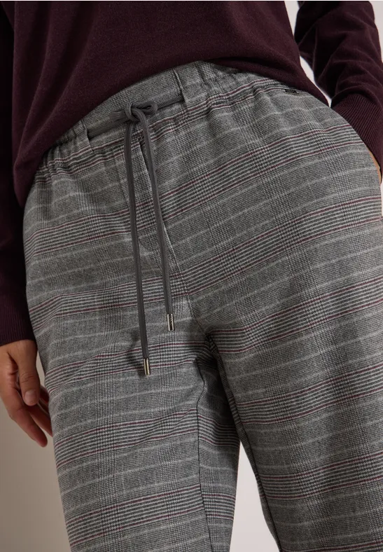 Detail einer grauen, karierten Hose mit Kordelzugbund, getragen zu einem burgunderfarbenen Pullover.