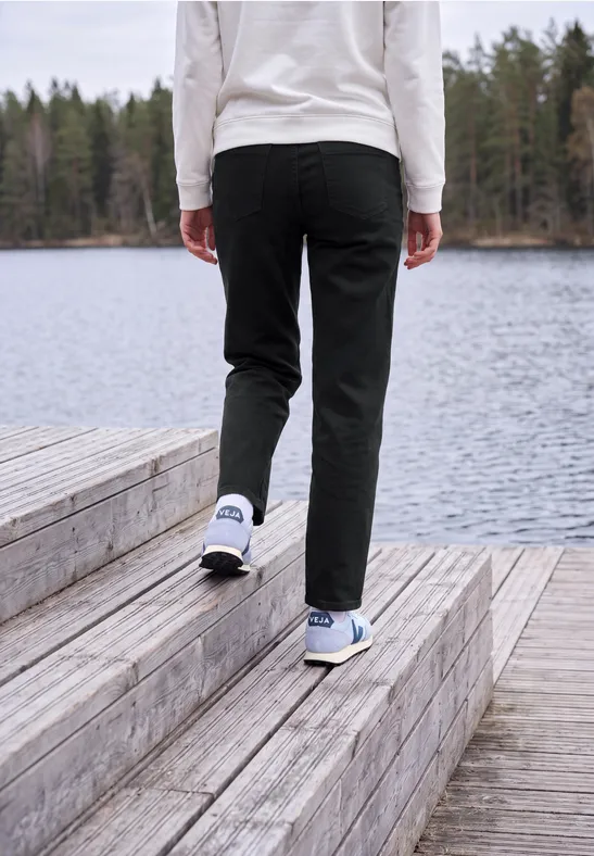 Person in schwarzer Hose und weißen Turnschuhen geht über eine Holzplattform am See.