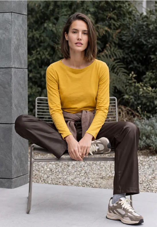 Frau in gelbem Pullover und brauner Hose sitzt entspannt auf einem Outdoor-Stuhl