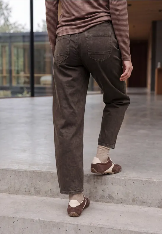 Eine Person in braunen Cordhosen und braunen Sneakern mit weißen Socken steigt eine Treppe hoch in modernem Umfeld.