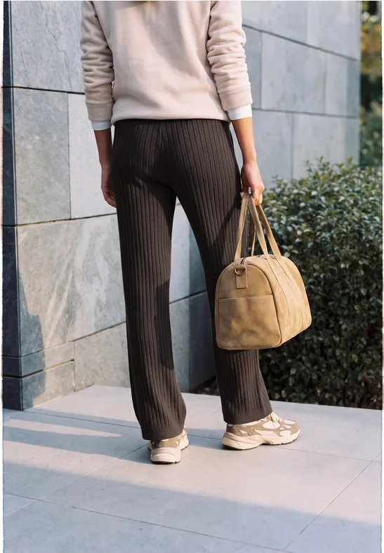 Une personne porte un pantalon à fines rayures, des baskets blanches et tient un sac à main jaune.