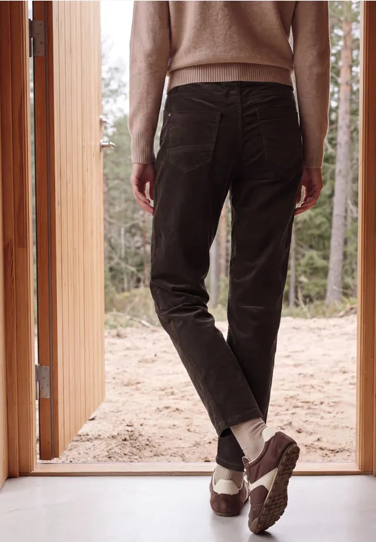 Eine Person steht in offen stehender Tür, trägt braune Hose, weiße Socken und robuste Schuhe, Blick in den Wald.