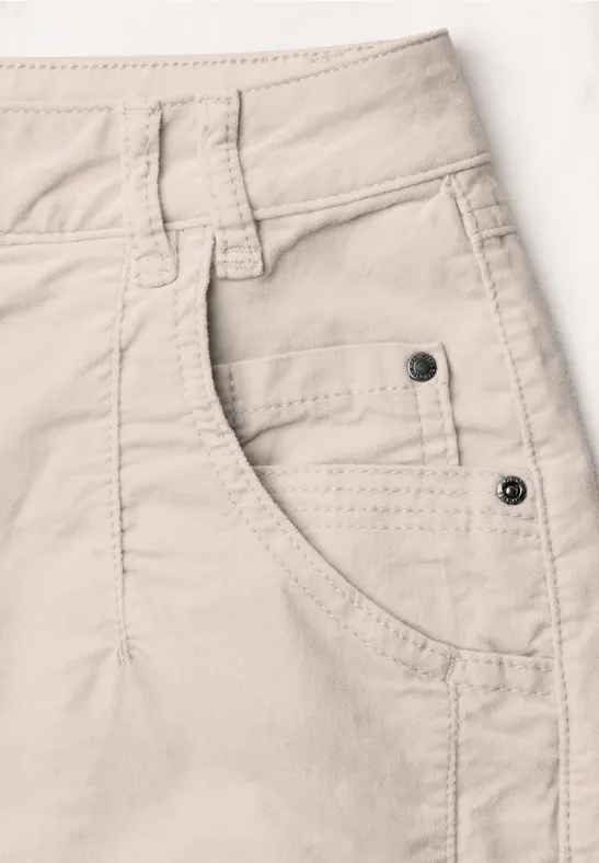 Beige Jeans- oder Stoffhose mit sichtbarer Fronttasche, Gürtelschlaufe und Metallnieten.