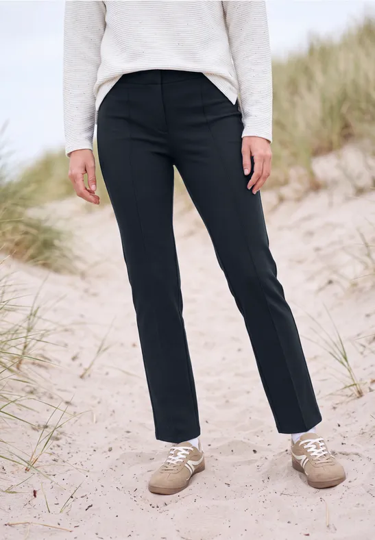 Personne en pantalon noir et chaussures beiges debout sur du sable près des dunes.