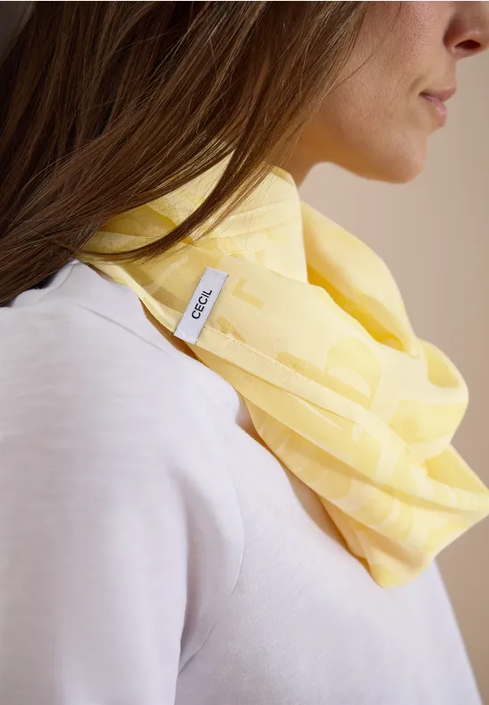 Person mit hellgelbem Schal um den Hals und hellem Oberteil, Gesicht unscharf.