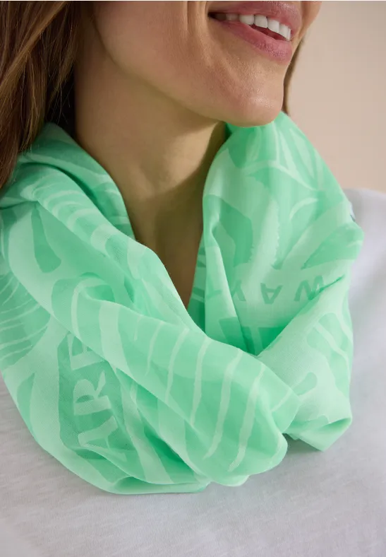 Eine Frau trägt einen neon-grünen Rundschal mit feinem Muster über einem weißen Oberteil.