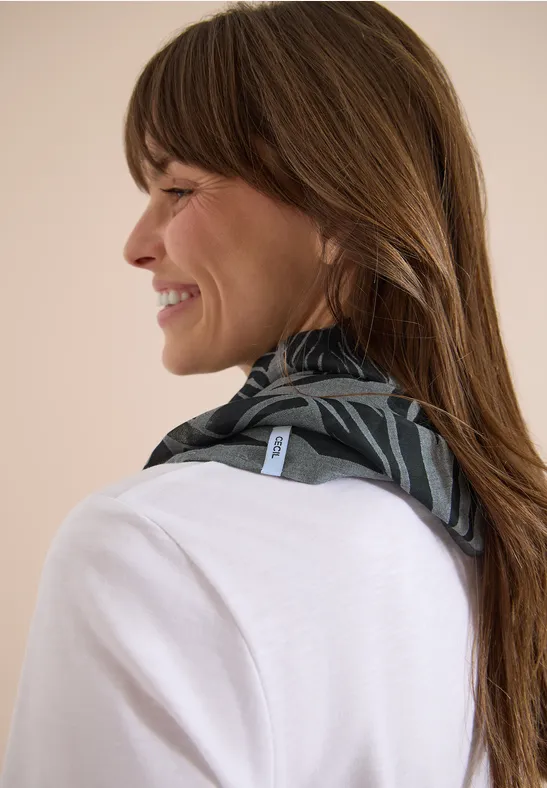 Eine Frau mit braunen Haaren trägt ein schwarzes, gemustertes Tuch um den Hals, das Gesicht ist verschwommen.