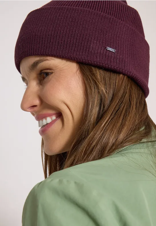 Gros plan d'une femme souriante en veste verte et bonnet violet.