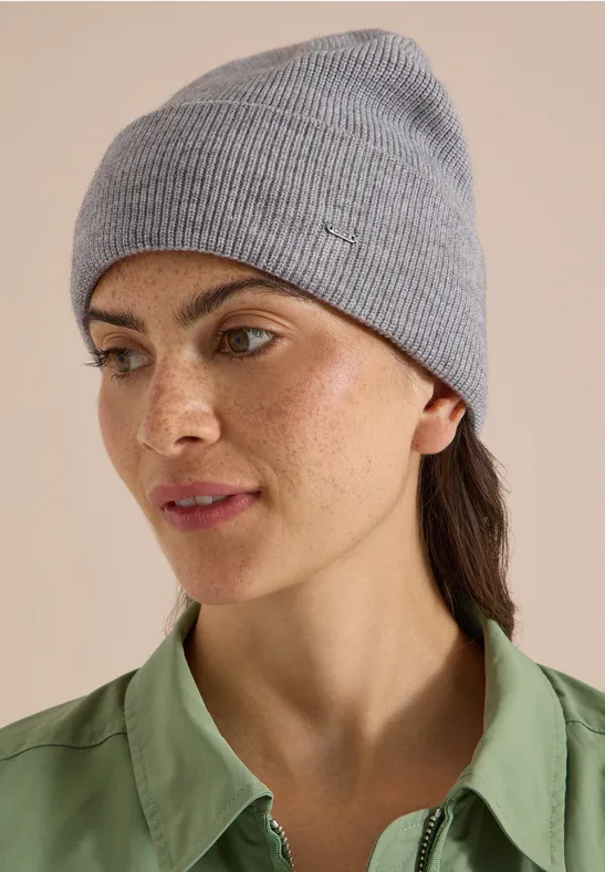 Une femme porte un bonnet gris et une chemise verte, regard de profil.