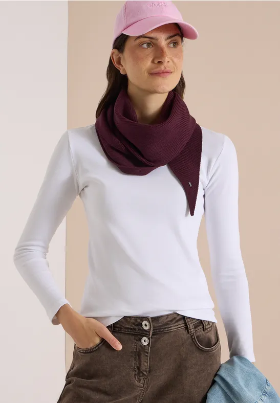 Femme avec tee-shirt à manches longues blanc, pantalon beige, foulard violet et casquette rose, tenant un pull bleu