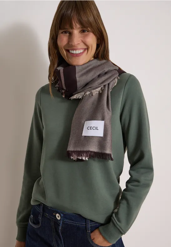 Femme souriante vêtue d’un pull vert et d’une écharpe grise.
