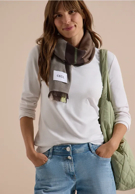 Jeune femme souriante en t-shirt blanc, jean, écharpe à carreaux et sac vert.