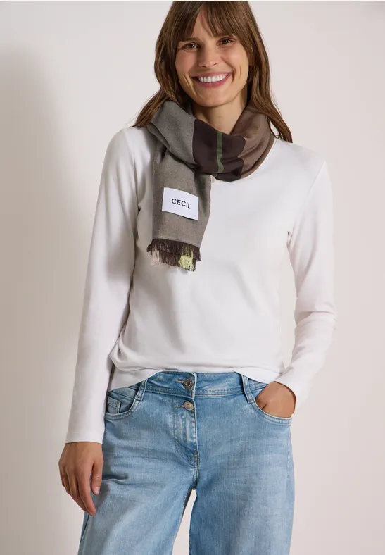 Une femme souriante porte un pull blanc, un jean bleu et une écharpe à carreaux.