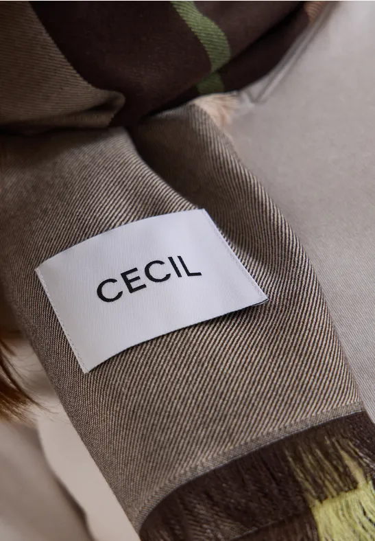 Gros plan d'un vêtement beige avec une étiquette blanche portant l'inscription noire CECIL.