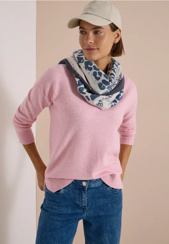 Frau in rosa Pullover, Jeans, Cap und blau-weiß gemustertem Schal