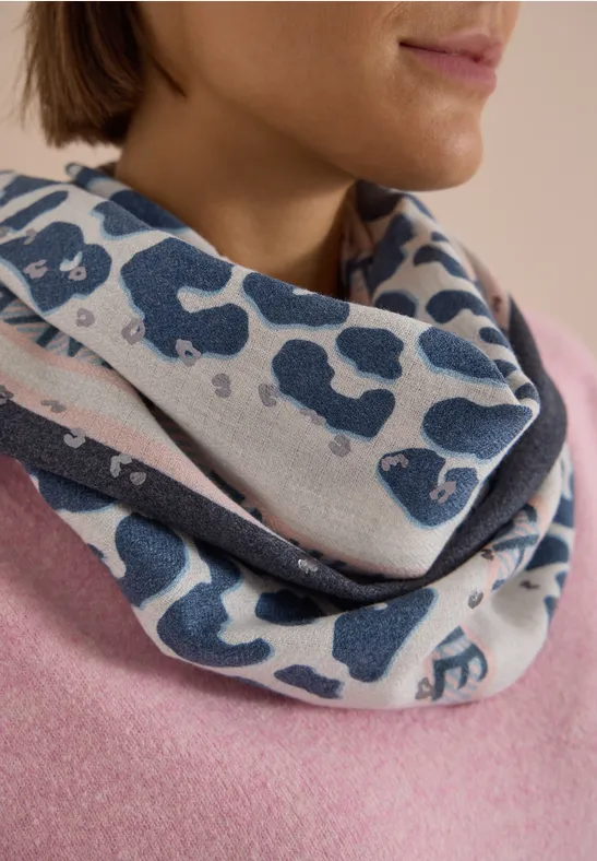 Eine Frau trägt einen lässigen Loop-Schal mit blauem Leopardenmuster über einem rosa Pullover.