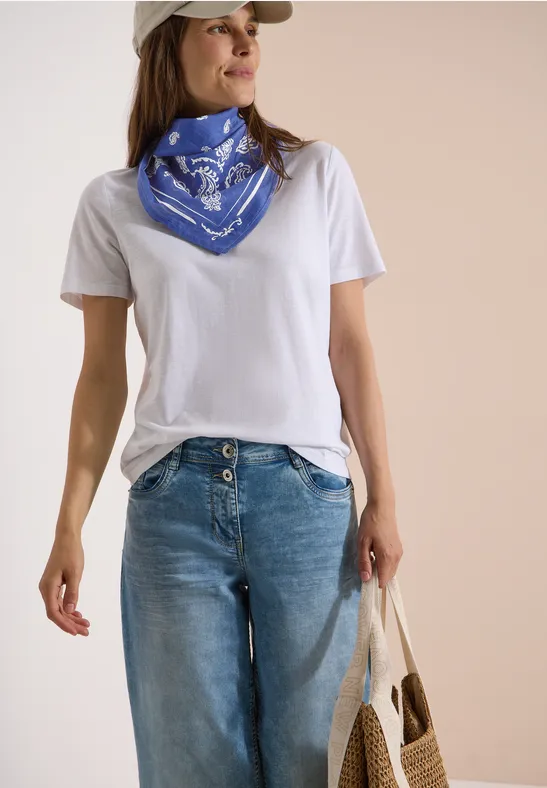 Frau trägt weißes T-Shirt, blaue Bandana am Hals, weite Jeans und hält eine Stofftasche.