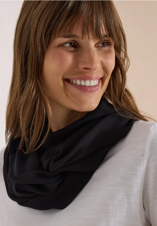 Femme souriante aux cheveux bruns, portant un col tube noir et un haut blanc.