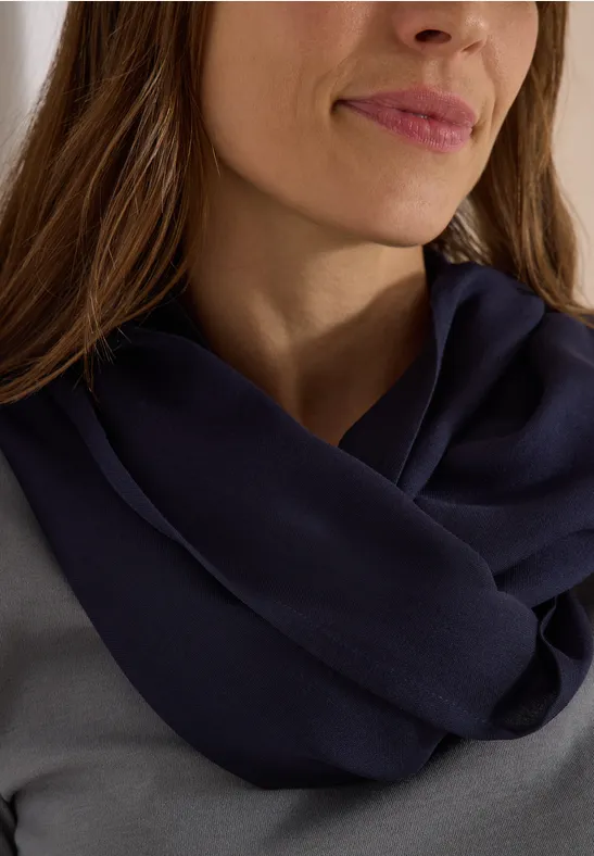Eine Frau mit langen braunen Haaren trägt einen dunkelblauen, rundgestrickten Schal über einem grauen Oberteil.