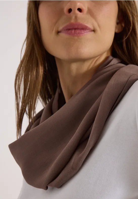 Gros plan d'une femme portant un foulard marron doux autour du cou et un haut blanc.