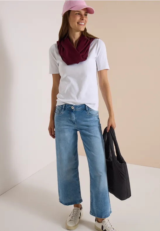 Femme en t-shirt blanc, casquette rose, foulard bordeaux, jean large, baskets blanches et grand sac noir.