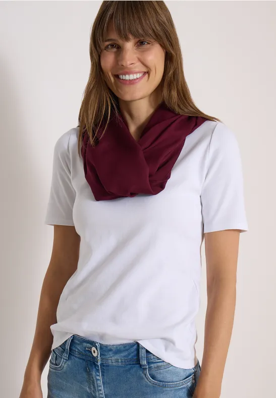 Femme souriante en t-shirt blanc, jean bleu et foulard grenat.