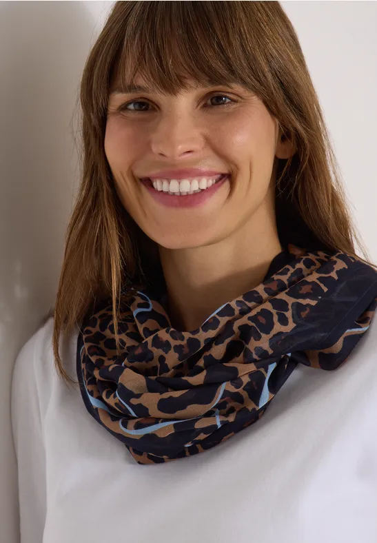 Portrait d'une femme souriante aux cheveux bruns, portant un haut blanc et une écharpe infinie léopard bleu et marron.