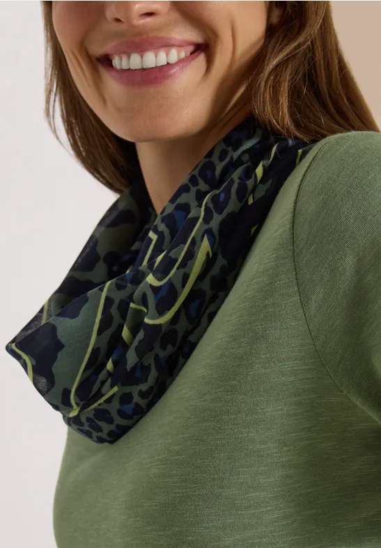 Femme souriante en haut vert et tour de cou vert foncé à motif léopard.