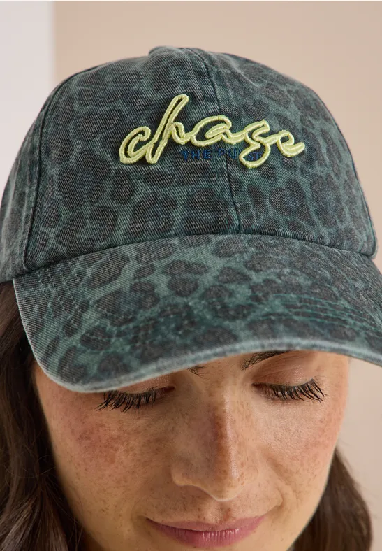 Person mit grün gemustertem Cap mit chase-Logo und Sommersprossen blickt nach unten.
