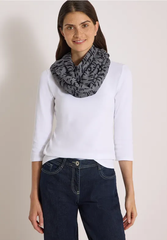 Femme en t-shirt à manches longues blanc, jean foncé et écharpe tube grise et noire.