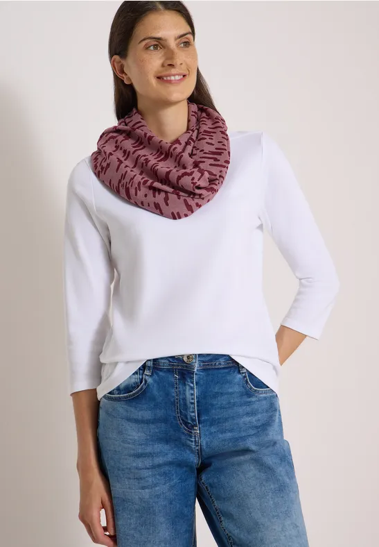 Femme en t-shirt blanc à manches longues, jean bleu et tour de cou rose à motif noir.