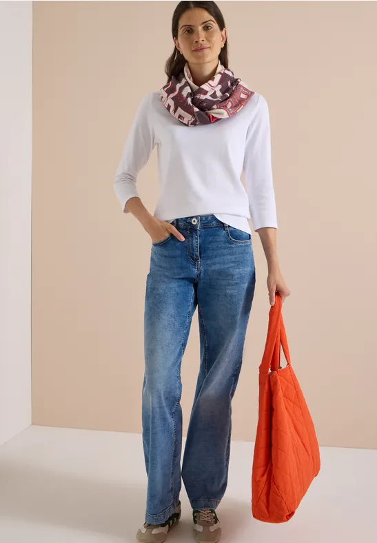 Femme en t-shirt blanc 3/4, jean ample et foulard imprimé, tenant un sac orange.