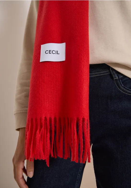 Écharpe rouge à franges avec étiquette "Cecil", portée sur un pull beige et un jean.