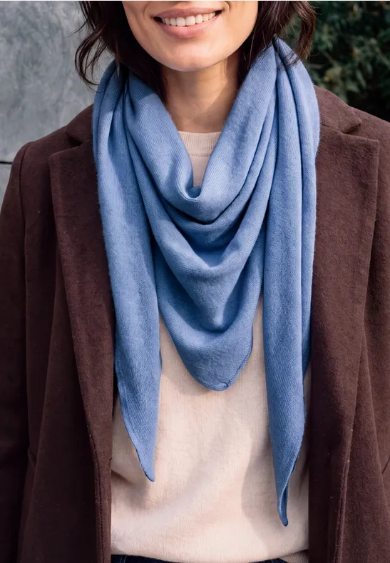 Frau in braunem Mantel, beigem Pullover und blauem, dreieckig drapiertem Schal.