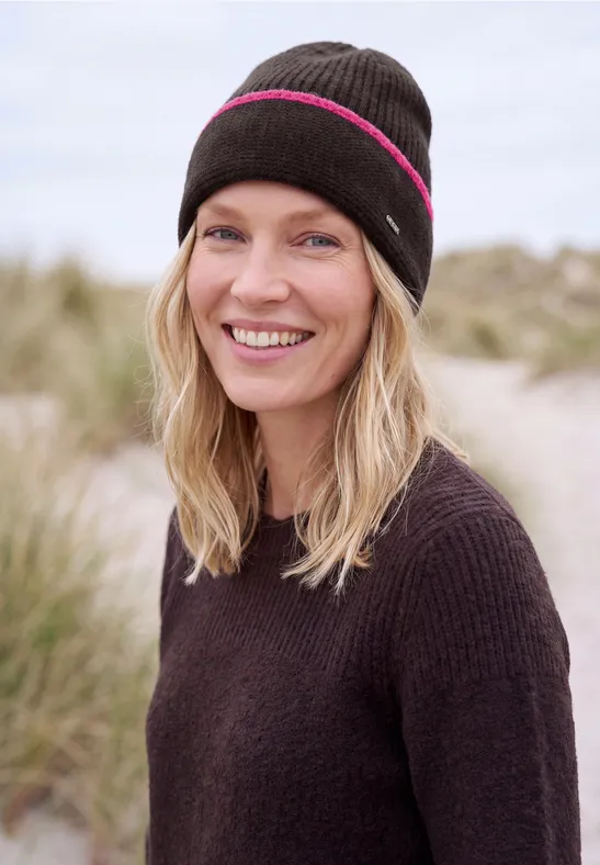 Eine lächelnde Frau mit Mütze steht am Strand vor Dünen.