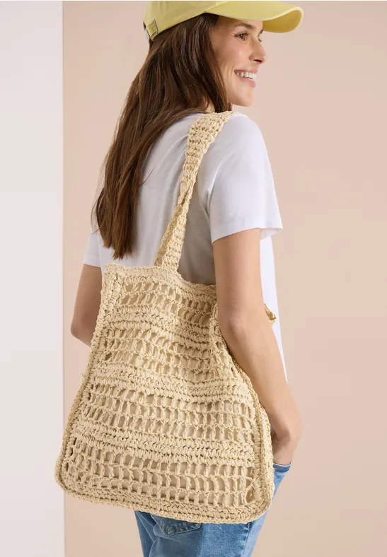 Frau von hinten trägt weißes T-Shirt und eine gehäkelte Strohtasche über der Schulter.