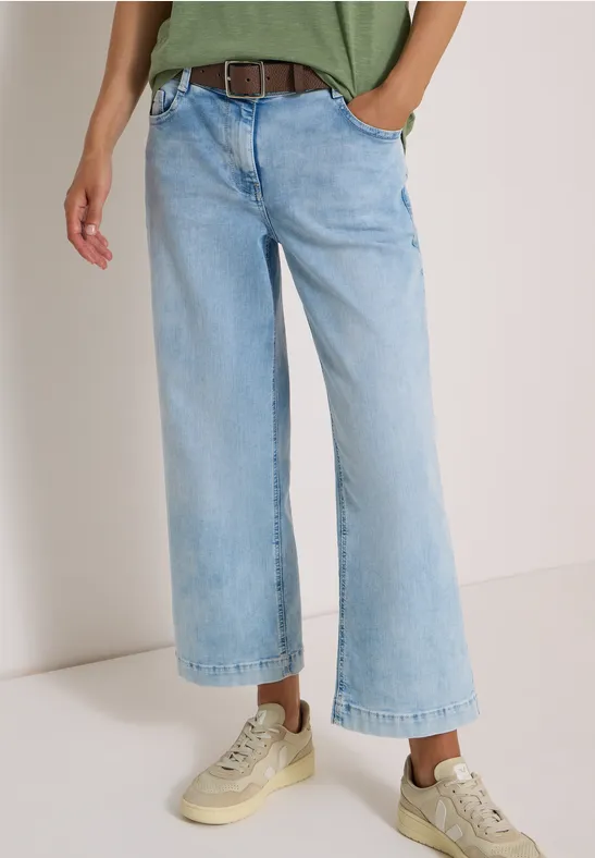 Frau trägt hellblaue, lässige, weit geschnittene 7/8-Jeans und helle Sneaker.