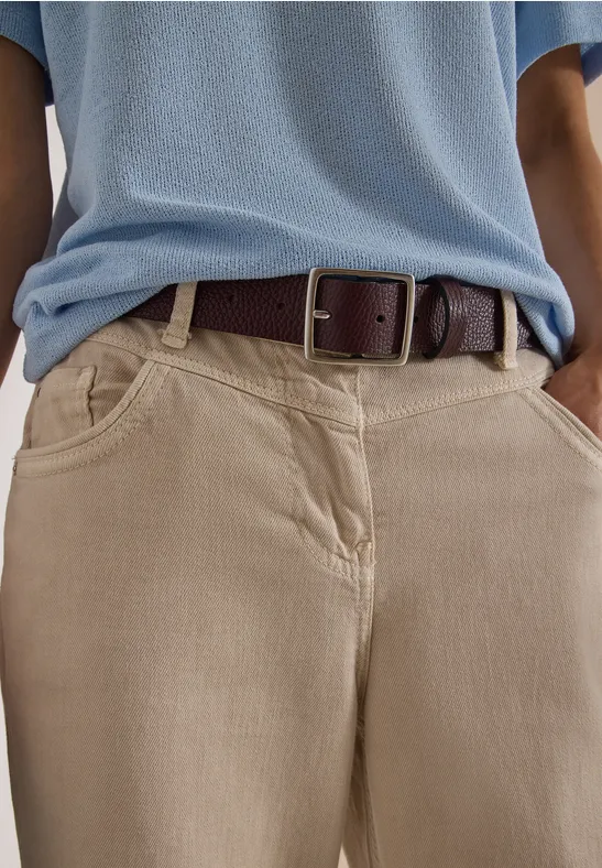 Person trägt beige Hose mit Taschen, hellblaues Shirt und braunen Ledergürtel